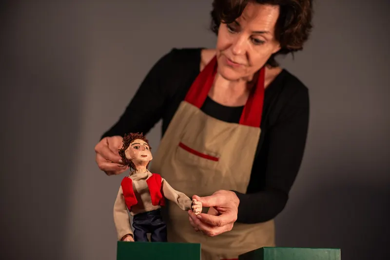 Manipuladora observa de perto o boneco que segura, ajustando a posição da cabeça e do braço antes da cena.